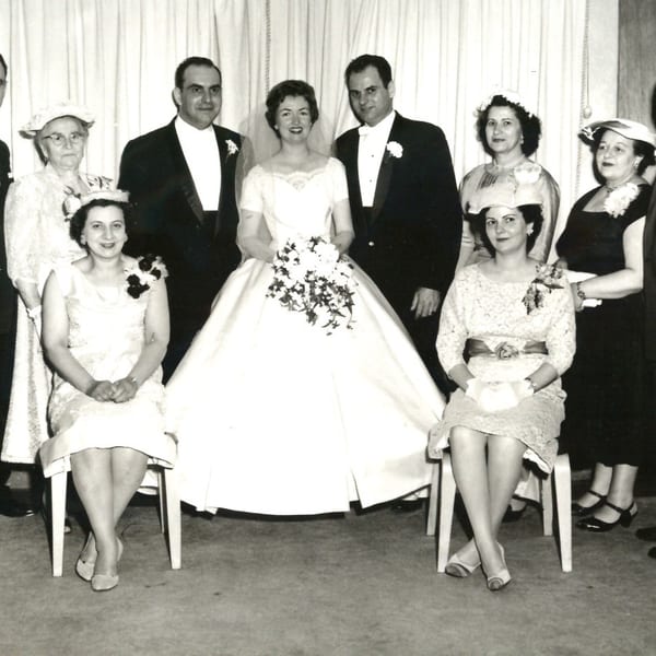 A black and white photo of a wedding party with the bride and groom surrounded by guests.