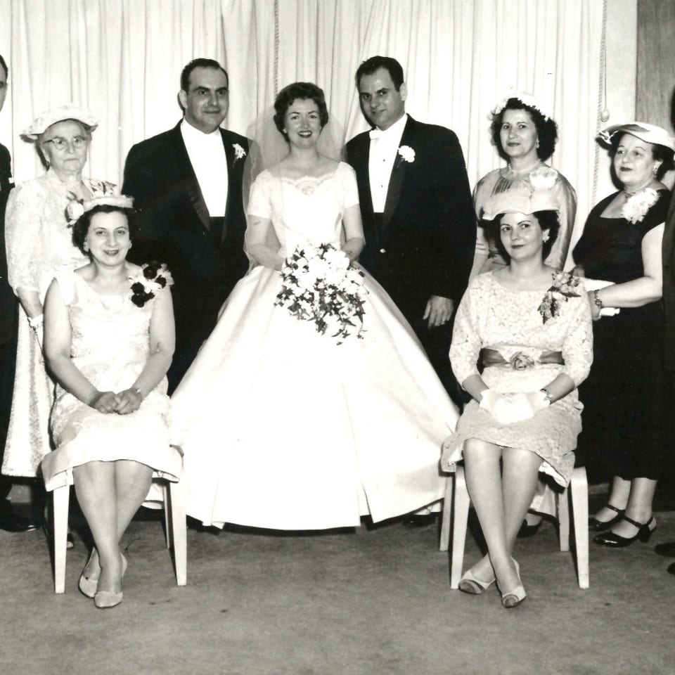 A black and white photo of a wedding party with the bride and groom surrounded by guests.
