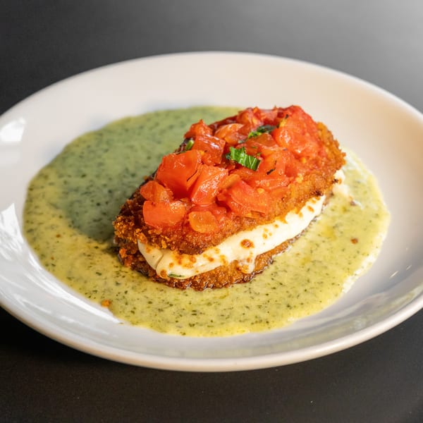 Crispy fried chicken topped with diced tomatoes and basil, served on a bed of green sauce.