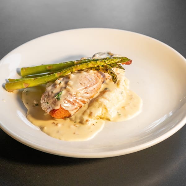 Pan-seared salmon with creamy sauce, mashed potatoes, and asparagus on a white plate.
