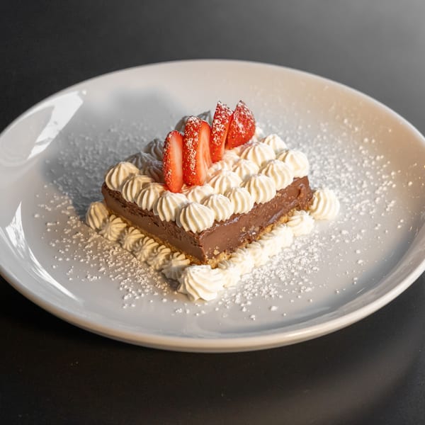 Chocolate tart with whipped cream and sliced strawberries, dusted with powdered sugar on a white plate.