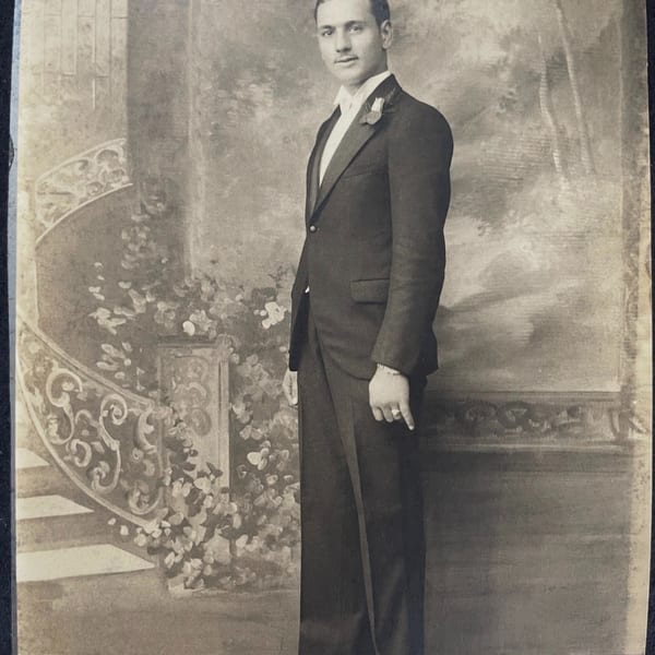 A vintage black and white portrait of a man in a tuxedo standing next to a painted staircase.