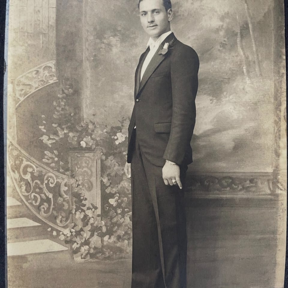A vintage black and white portrait of a man in a tuxedo standing next to a painted staircase.