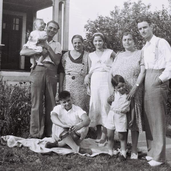 A black and white photo of a family of eight posing outdoors in front of a house.