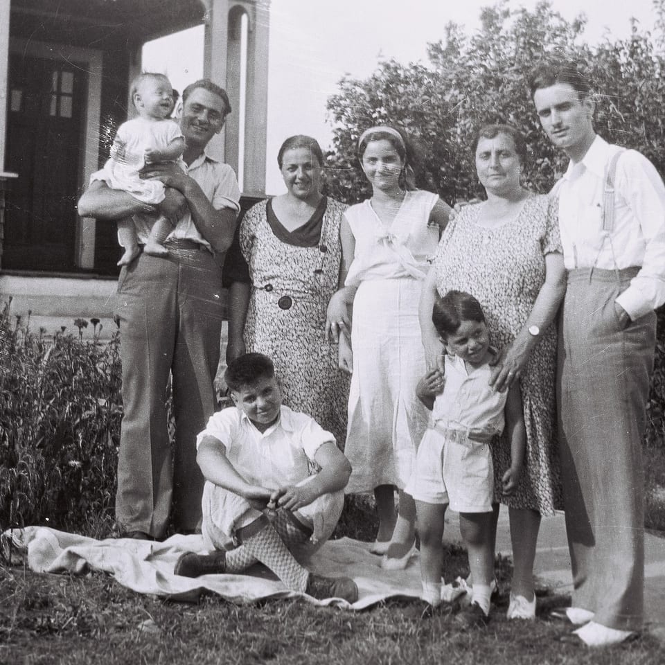 A black and white photo of a family of eight posing outdoors in front of a house.