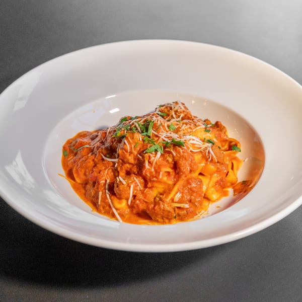 Pappardelle pasta with meatballs, red sauce, parmesan cheese, and parsley in a white bowl.
