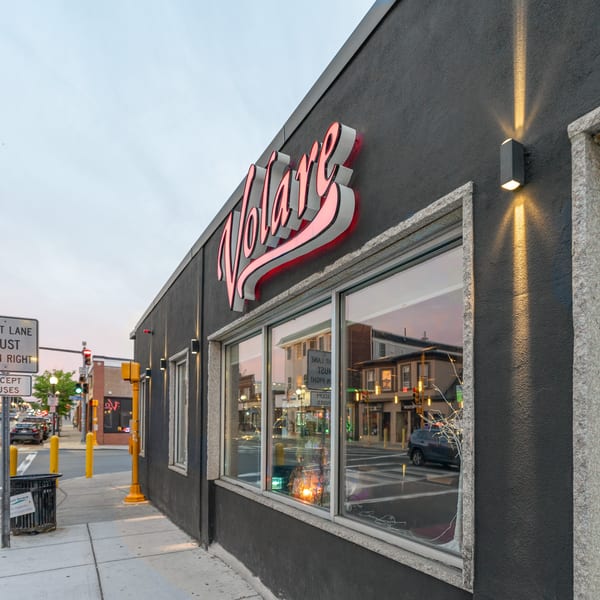 Exterior of Volare restaurant at dusk, with a glowing red sign and street reflections in the windows.