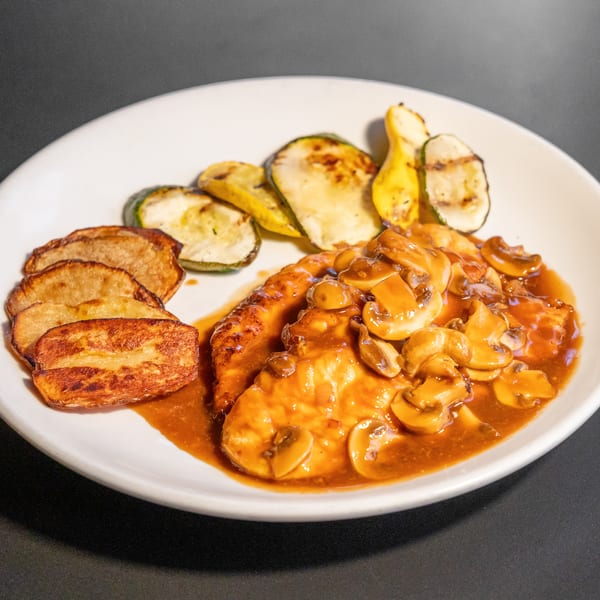 Chicken with mushroom sauce, roasted potatoes, and grilled zucchini on a white plate.