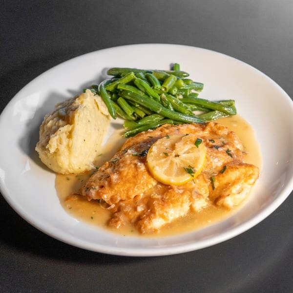 Lemon butter fish with mashed potatoes and green beans on a white plate.