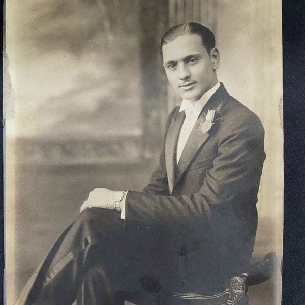 A vintage sepia portrait of a man in a tuxedo with a boutonnière, seated and looking at the camera.