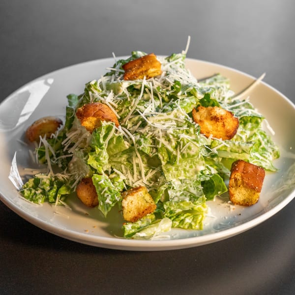 A Caesar salad with romaine lettuce, croutons, and shredded Parmesan cheese on a white plate.